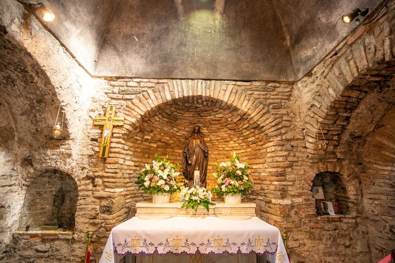 Na Turquia existem diversos locais históricos e marcantes para muitas religiões, sendo a maioria rotas cristãs, na região do mar Egeu, onde encontra-se uma das paradas mais buscadas pelos peregrinos: a Casa da Virgem Maria. O roteiro religioso no destino ainda conta com a Basílica de São João, a Caverna dos Sete Adormecidos, as Sete Igrejas do Apocalipse, entre outros lugares.  Casa da Virgem Maria em Éfeso  Historicamente, após a crucificação de Jesus em Jerusalém, o apóstolo João levou Maria à Éfeso, uma importante cidade costeira. Naquela época, a região estava sob o domínio do Império Romano, então João levou a mãe de Cristo para um local isolado em uma floresta na encosta da montanha Bülbül.  A descoberta da Casa da Virgem Maria ocorreu por meio de uma freira alemã, Beata Anne Catherine Emmerich. Embora a freira tenha morrido em 1824, as imagens descritas por ela permitiram aos padres lazaristas determinar a localização da casa onde a Virgem Maria passou seus últimos dias. Nos anos seguintes, o local foi aceito como rota de peregrinos e, em 1951, o Papa Pio XII concedeu à Casa da Virgem Maria o status de Lugar Santo e local de peregrinação católica. A partir dessa declaração, iniciou-se um fluxo de visitantes que é considerado sagrado e restaurado pelos muçulmanos. Os Papas Paulo VI e João Paulo II estão entre os líderes religiosos que já estiveram em Éfeso para visitar a casa e prestar homenagens à Virgem Maria.    Neste templo sagrado, as cerimônias são tradicionalmente realizadas no dia 15 de agosto, que é considerada a data da ascensão da Virgem Maria ao céu, aos 101 anos, que depois foi sepultada pelo apóstolo João em uma das montanhas da região.     A Casa da Virgem Maria fica no distrito de Selçuk, em Izmir e, após sua descoberta, foi convertida em uma igreja que recebe seus visitantes com uma estátua da mãe de e uma piscina batismal, no interior do templo existe uma representação de Maria retratada pelo pintor Ratislas Loukine. A Casa pode ser visitada juntamente com a Fonte Sagrada adjacente e a histórica Parede dos Pedidos. Muitas pessoas acreditam que a água que sai da fonte é potável e tem poderes curativos, por isso, alguns visitantes até enchem suas garrafas. A parede é enfeitada com guardanapos e papéis, nos quais os visitantes podem escrever seus pedidos e orações.     Outros locais da Rota Sagrada Na região encontra-se também a Caverna dos Sete Adormecidos, onde, de acordo com a história, sete jovens cristãos que viviam durante o reinado do imperador romano Décio se recusavam a realizar rituais pagãos e a oferecer sacrifícios ao templo. Enfrentando ameaças de morte, os sete rapazes se refugiaram na caverna perto de Éfeso e, por ordem do imperador, uma parede foi construída na entrada da caverna impedindo, assim, que os sete amigos escapassem e fazendo com que eles caíssem em sono profundo. Quando acordaram, 200 anos depois, descobriram que o Cristianismo era a religião do estado e Teodósio II era o imperador atual. Conta-se que, após a morte dos sete jovens, houve um grande funeral e uma igreja foi erguida sobre a caverna onde foram enterrados. Durante as escavações na Caverna dos Sete Adormecidos, uma igreja foi descoberta, junto com numerosas tumbas e inscrições sobre os jovens.     Como desenvolvimentos marcantes na história do cristianismo ocorreram nessas terras antigas, atualmente a Turquia abriga alguns dos assentamentos mais importantes e sagrados do mundo, bem como igrejas e monumentos. As estruturas e cenários desses marcos históricos do cristianismo também são considerados centros de peregrinação.     Outras rotas de peregrinação dos cristãos no país incluem a Igreja Hatay St. Pierre, considerada a primeira catedral do mundo, onde a comunidade que se definiu como cristã pela primeira vez na história foi celebrada e St. Pierre foi nomeado o primeiro Papa. Também nas rotas de peregrinação estão a Igreja de São Nicolau, na cidade de Demre (Antalya), onde São Nicolau, também conhecido como Papai Noel, serviu como bispo.    A região da Capadócia conta com cerca de 30 cidades subterrâneas esculpidas nas rochas, onde os primeiros cristãos se esconderam enquanto fugiam da perseguição do Império Romano. Estima-se que tenham mais 200 cidades embaixo da terra que ainda não foram exploradas na localidade.    Mais ao leste do país, está a Igreja Van Akdamar, uma catedral apostólica armênia medieval construída como uma igreja palatina para os reis de Vaspuracânia, que foi erguida para preservar um pedaço da cruz na qual Jesus foi crucificado.    Em Iznik, localizada na província de Bursa, existe outra mesquita com nome de Hagia Sophia, uma antiga igreja bizantina onde foram realizados o primeiro e o sétimo concílios ecumênicos -- o Primeiro e o Segundo Concílio de Nicéia.